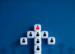 A visual representation of an organizational structure, composed of white dice forming a hierarchical shape on a blue background, with black and red person icons symbolizing the hierarchy.